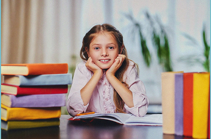 A young girl sitting at a table surrounded by stacks of engaging childrens books, with a big smile on her face indicating her love and excitement for reading