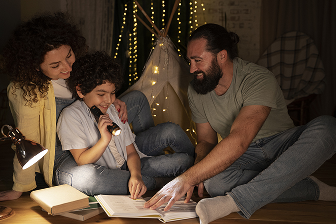 Dad, Mom and Son Reading a Book with a Flashlight